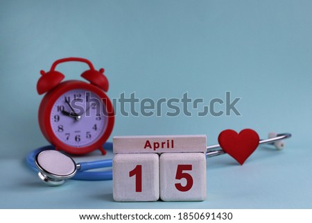 April 15st. White wooden calendar blocks with date, clock and stethoscope on a blue pastel background. Selective focus. health concept