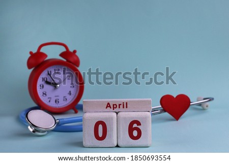 April 6st. White wooden calendar blocks with date, clock and stethoscope on a blue pastel background. Selective focus. health concept
