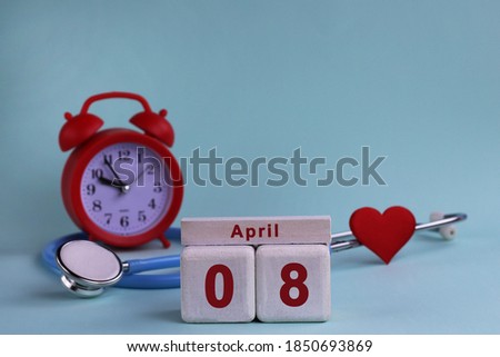 April 8st. White wooden calendar blocks with date, clock and stethoscope on a blue pastel background. Selective focus. health concept