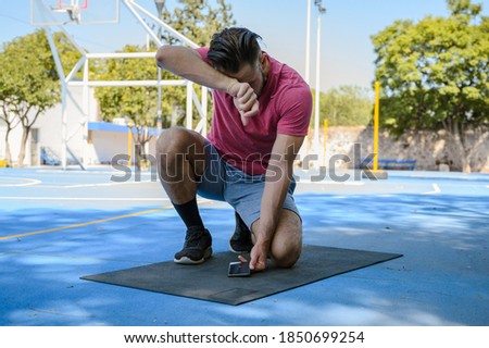 Fitness man resting at the park watching videos and using cellphone. White handsome man preparing to workout outside in a sunny day.