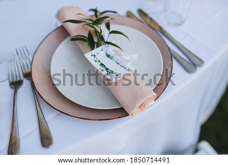 Plate, paper napkin, forks, knife, invitation with the name lie on the table with a white tablecloth. Special food accessories, dishes, decorations. Wedding photography, concept.