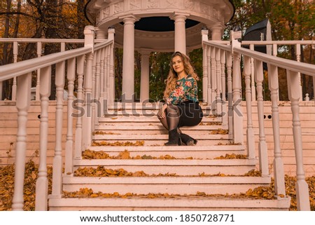 A beautiful girl stands a young with a charismatic appearance blonde in a colored shirt, against the background of the steps laughter autumn haircut embrace