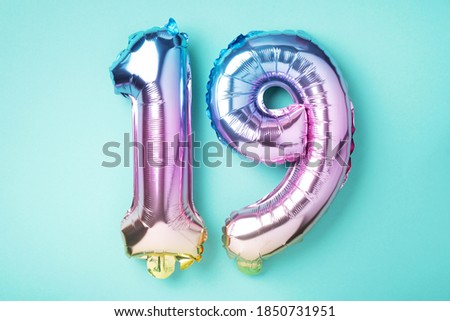 Creative layout. Rainbow foil balloon number, digit nineteen. Birthday greeting card with inscription 19. Anniversary concept. Top view. Stylish colored numeral on blue background. Numerical digit.