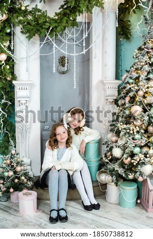 two cute sisters open presents by the new year tree. garland, cozy cute holiday atmosphere. school holidays for children. the girls are happy.