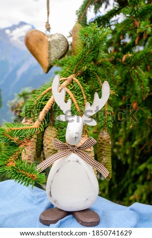 Green Christmas tree with cones growing in French Alps mountains decorated with hanging wooden heart  and christmas moose and mountain peaks on background
