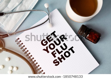 Inscription -GET YOUR FLU SEASON. Written in a notepad to remind you of what's important. Top view of the table along with a stethoscope and a mask. Health care concept.