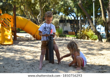 On a sandy playground, a boy  looks at a smartphon the girl is playing on the playground. Children's addiction to the cell phone, new technologies and social networks. 