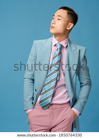 Handsome Asian guy in suit on a blue background straightens his jacket and pink trousers close-up cropped view