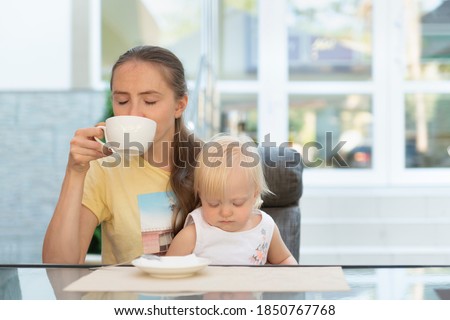 Young mother is enjoying coffee in cafe while child is playing in her arms