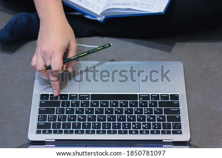A woman works remotely from home, typing on her computer, holding a green pencil in her hand and an open diary on her lap.