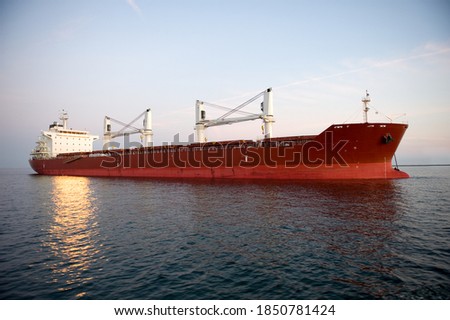 A red shipping transportation freighter anchored just inside a port of call.