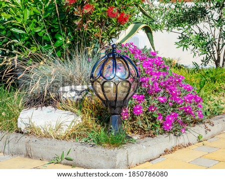 Low round decorative lantern at the corner of a flower bed with flowers and bushes
