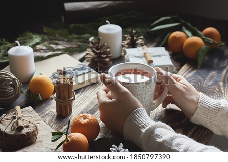 Woman drinks hot tea while preparing gift packages on wooden table. Chic cozy craft gift boxes. Natural aestetic. Zero waste, plastic free, trendy hand made gift package for Christmas.