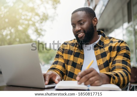 Young handsome African American man using laptop computer, taking notes, planning start up, working online. Portrait of happy student studying, learning languages, online education concept
