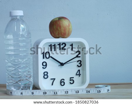Photo of alarm clock with an apple,water bottle and measure tape isolated on white background.Diet and healthy concept.Selective focus.