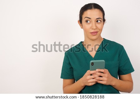Funny Young arab doctor surgeon woman over isolated white background holds telephone hands reads good youth news look empty space advert 