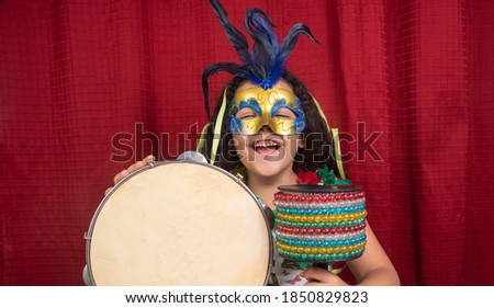 Little girl with mask and streamers and carnival instruments from Brazil, red background, selective focus.
