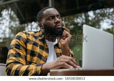 Portrait of pensive African business man using laptop computer, planning project, brainstorming at workplace. Serious student studying, exam preparation, searching solution, online education 