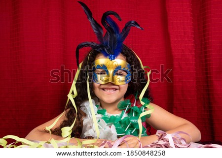 Small girl with mask and necklaces used in Brazil's carnival, red background, selective focus.