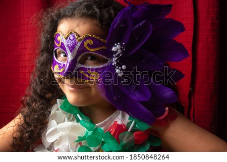 Small girl with mask and necklaces used in Brazil's carnival, red background, selective focus.