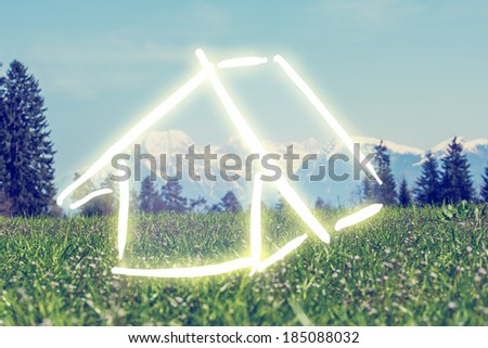 Hand-drawn house in white on a green field against a backdrop of a scenic mountain landscape, conceptual of a dream eco house and ownership. With retro filter effect.