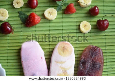Homemade strawberry cherry banana blueberry ice cream or popsicles decorated green mint leaves on teal rustic table, frozen fruit juice, vintage style, top view