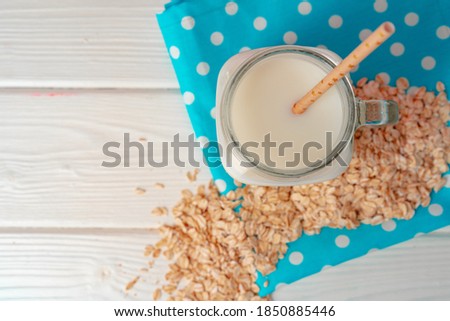 Glass jar of oat vegan milk with oat flakes on white wooden table
