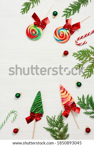 Christmas composition. Christmas sweets and candy canes, thuja branches, and New Year small red and green balls on white wooden table, top view, flat lay.