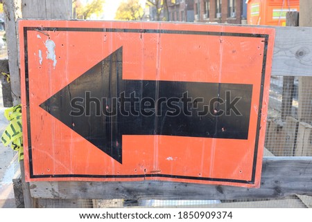 Orange Construction sign with black arrow pointing left outdoors