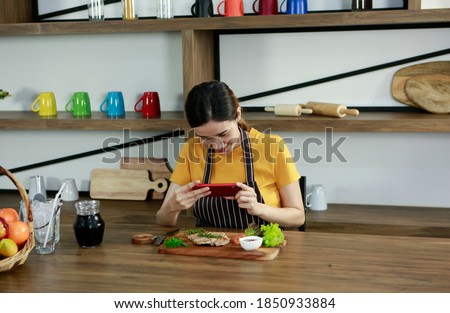 Young Asian pretty lady shooting picture of decorate meat steak food in plate by smartphone after cooking in kitchen while lunch time. Cook Food Salad Steak Delicious Chef Concept
