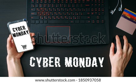 Woman's hands using laptop and smartphone for shopping online at home while Cyber Monday Sales. Top view of the workspace on black background. Promotion inscription on screen.