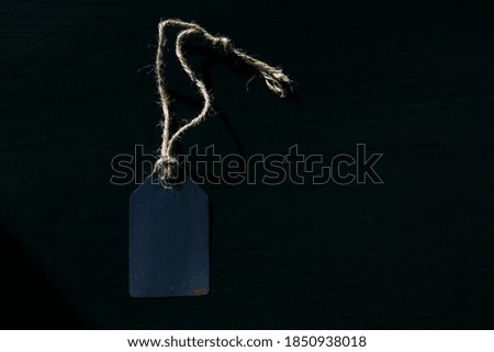 Concept of Black Friday. Empty label on a rope with space for text on black wooden background in sunlight.