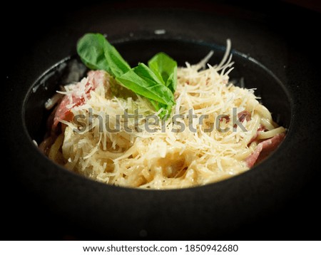 Classic Spaghetti carbonara is Italian Pasta with with a cream sauce, bacon and pepper and parmesan cheese on black background. Dark food photography style.
