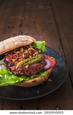 Burger with vegetarian hamburger patty, salad, tomatoes and roasted onions on a black plate on wooden table, vertical stock photo with copy space
