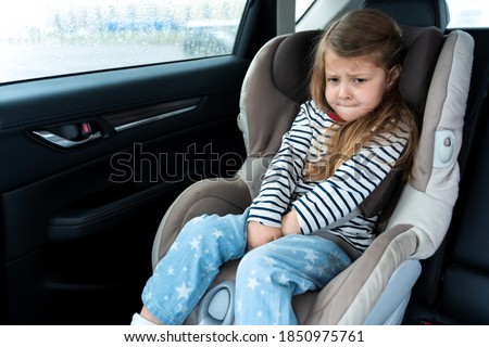 Little girl is driving in car. Kid child wants to go to toilet, pee and endures. Traveling, riding on road in safe baby seats with child belts. Fun family trip, activity with parents. Royalty-Free Stock Photo #1850975761