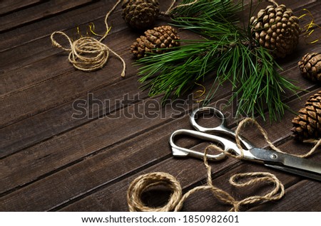Closeup of twine, scissors, green fir branches and cones on the brown wooden table.Empty space