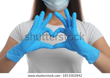 Woman in protective face mask and medical gloves making heart with hands on white background, closeup