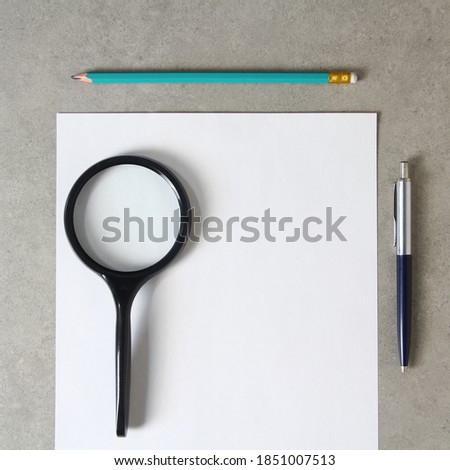 Template of white paper with a ballpoint pen, magnifying glass and simple pencil on light grey concrete background. Concept of new idea, business plan and strategy, development and implementation of