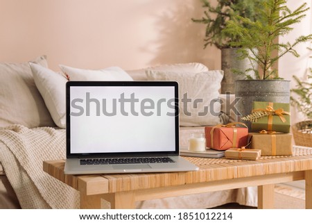 Laptop with blank screen mock up on table in stylish interior decorated for Christmas holidays. Winter holidays concept.