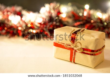 Christmas gift in a box wrapped in craft paper, tied with ribbon and rope, decorations with garland lights in a blur, red tinsel. New year. Background. Copy space
