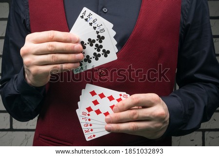 the croupier in a black shirt and red vest holds cards of black and red suit