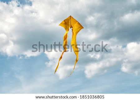 Yellow kite flying on blue sky background. Cloudy day summer scene. Freedom concept
