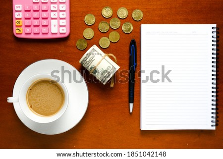 Flatlay picture of copyspace notebook, pen, milk coffee, fake cash, coins and calculator. Financial consultation and planning concept.