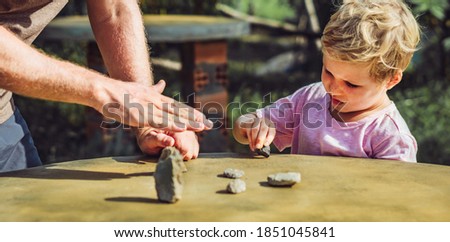 Father son play outside sun day, show explain driving traffic regulation rules use stone imitation cars. Instruction hand palm finger gesture. Expressive Serious face expression. Home child education