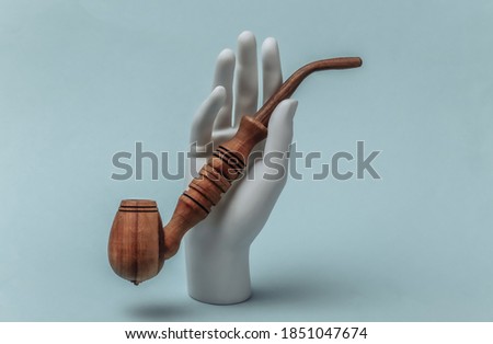 White mannequin hand holds smoking pipe on blue background