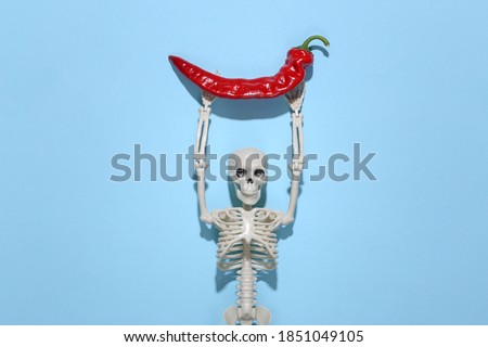Skeleton holds red chili pepper on a blue background