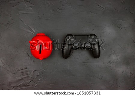 Red piggy bank with black joystick gaming controller on black background. Top view with copy space. Save money for your leisure time and buy games.