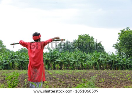 Young indian farmer in traditional wear and holding wooden stick in hand at field