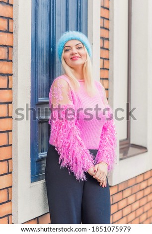 Nice blonde woman in pink sweater and blue wool hat, winter season. Women's outfits, fashionable concept