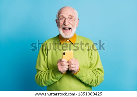 Photo of pensioner old man hold smartphone excited face wear glasses green sweater isolated blue color background